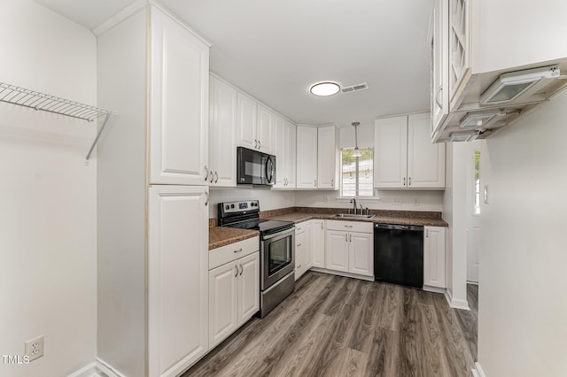 kitchen with black appliances, dark countertops, wood finished floors, white cabinets, and a sink