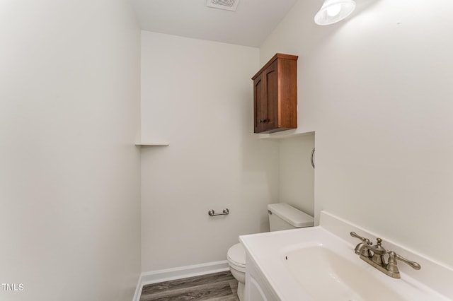 half bath with a sink, toilet, wood finished floors, and baseboards