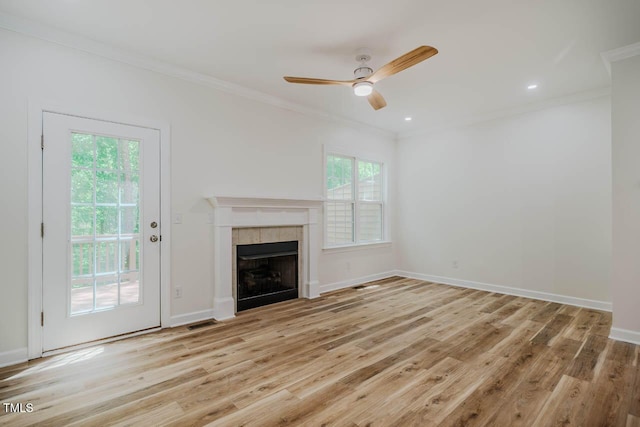 unfurnished living room with ornamental molding, a ceiling fan, light wood finished floors, a tile fireplace, and baseboards