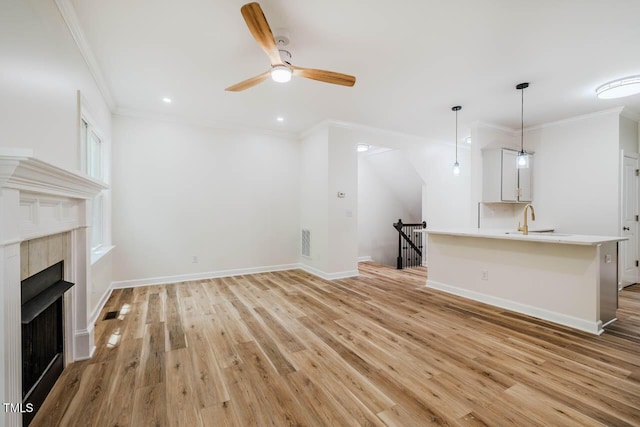 unfurnished living room featuring crown molding, a sink, light wood-type flooring, a ceiling fan, and a fireplace