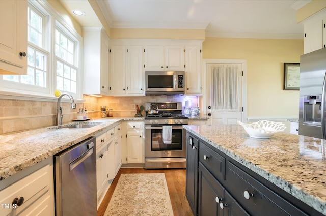 kitchen featuring stainless steel appliances, a sink, white cabinetry, dark cabinets, and light stone countertops