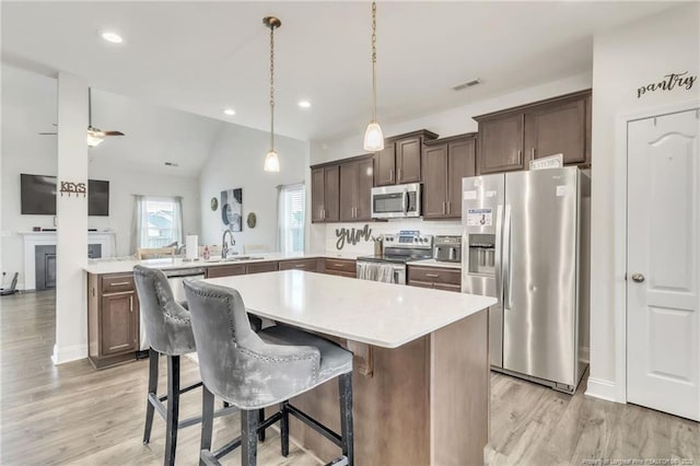 kitchen featuring appliances with stainless steel finishes, dark brown cabinetry, a peninsula, light countertops, and light wood finished floors