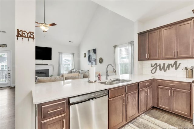 kitchen with stainless steel dishwasher, a sink, a peninsula, light wood-style flooring, and open floor plan