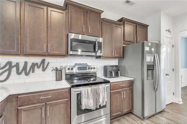 kitchen with stainless steel appliances, light wood-style flooring, backsplash, and light countertops