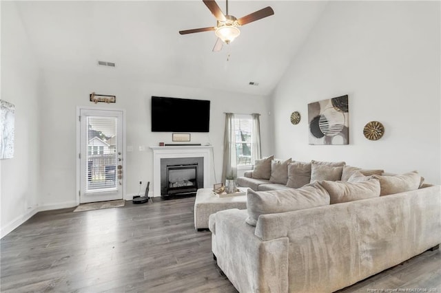 living room with healthy amount of natural light, high vaulted ceiling, ceiling fan, a glass covered fireplace, and wood finished floors