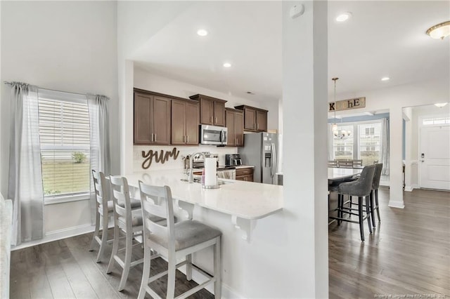 kitchen featuring appliances with stainless steel finishes, a kitchen bar, light countertops, dark wood finished floors, and plenty of natural light