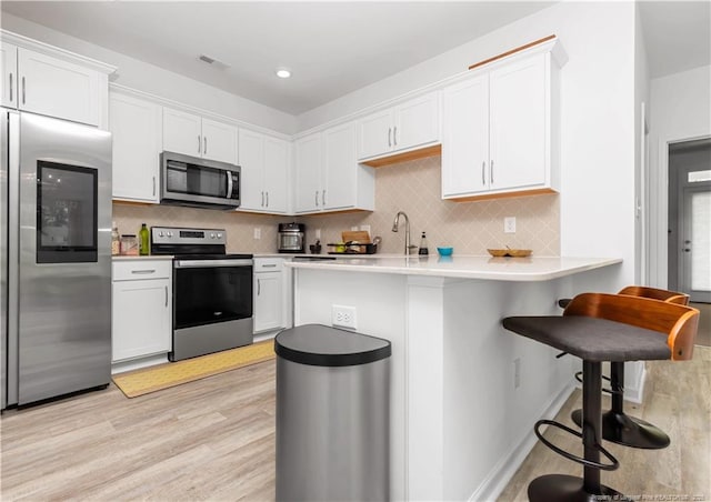 kitchen with appliances with stainless steel finishes, light wood finished floors, a breakfast bar, and white cabinets