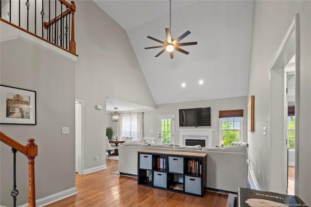 living room featuring high vaulted ceiling, ceiling fan, stairs, a fireplace, and wood finished floors