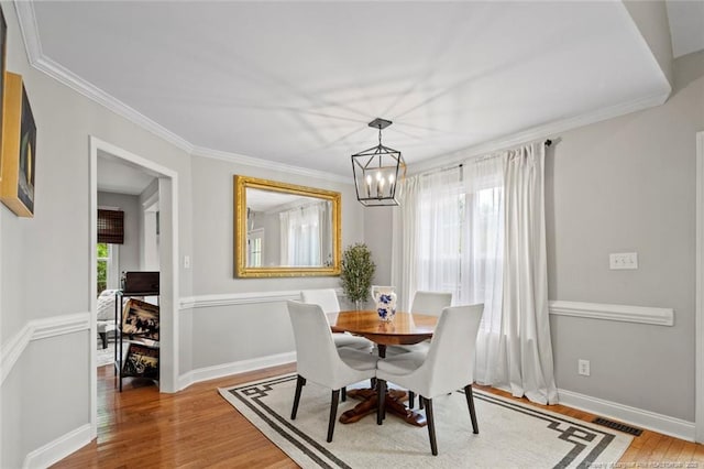 dining area featuring wood finished floors, a chandelier, crown molding, and baseboards