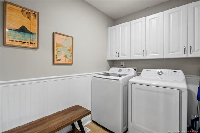 clothes washing area featuring cabinet space, washing machine and dryer, and a wainscoted wall