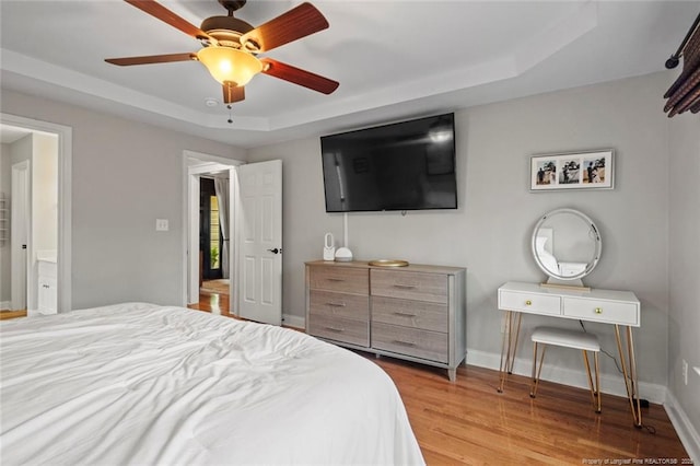 bedroom with a tray ceiling, wood finished floors, and baseboards