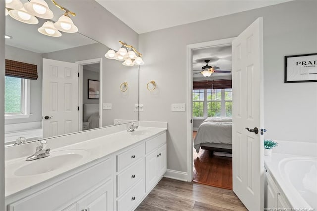 ensuite bathroom featuring double vanity, baseboards, a bath, wood finished floors, and ceiling fan