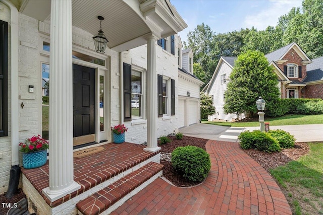 doorway to property featuring a porch, concrete driveway, a garage, and brick siding