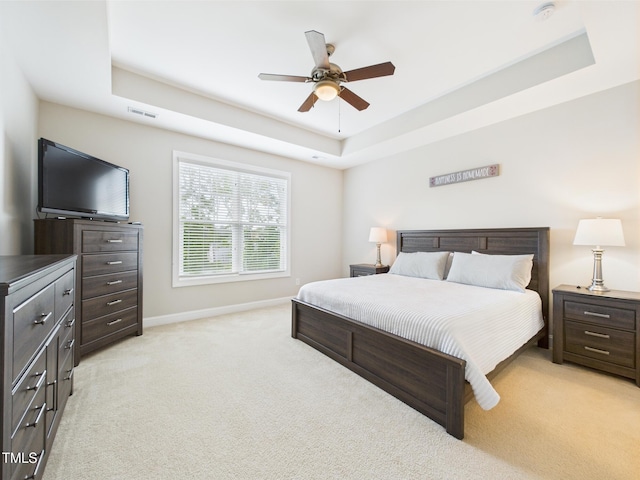 bedroom featuring a raised ceiling, light colored carpet, baseboards, and ceiling fan