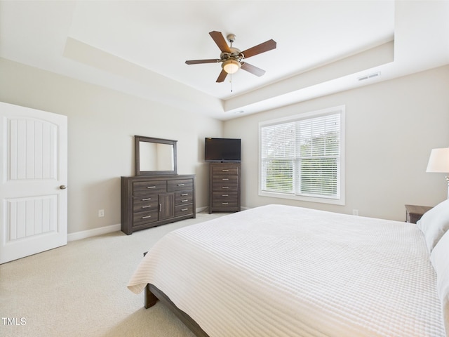 bedroom featuring a raised ceiling, light carpet, baseboards, and ceiling fan