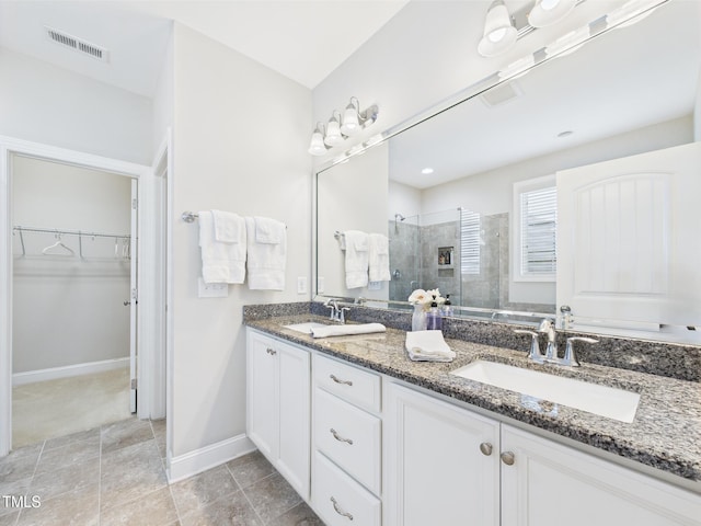 full bath with a stall shower, a walk in closet, double vanity, and baseboards