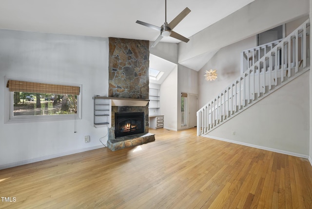 unfurnished living room featuring stairway, wood finished floors, a stone fireplace, a ceiling fan, and high vaulted ceiling