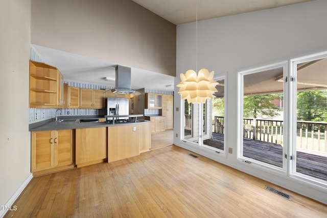 kitchen with open shelves, light wood-style floors, stainless steel fridge, a sink, and a peninsula