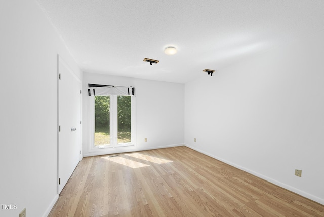 unfurnished room featuring light wood-type flooring, baseboards, and a textured ceiling