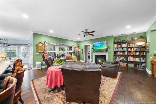 living area with crown molding, a ceiling fan, a glass covered fireplace, hardwood / wood-style floors, and baseboards