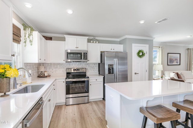 8615 Kenridge Ln, Fuquay Varina, NC 27526 - kitchen with appliances with stainless steel finishes, a sink, ornamental molding, backsplash, and a kitchen breakfast bar
