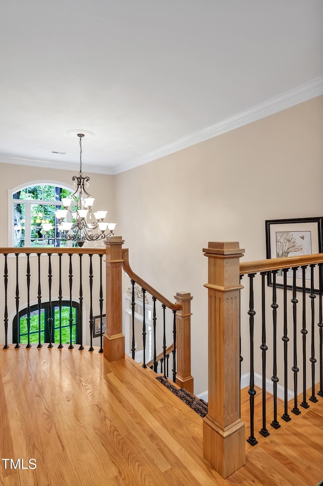 stairway with wood finished floors, ornamental molding, a chandelier, and baseboards