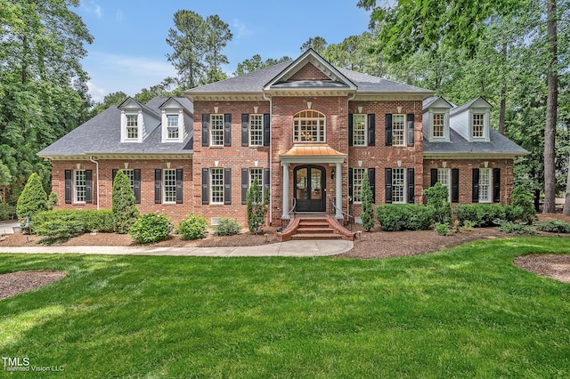 colonial-style house featuring a front yard, brick siding, a shingled roof, and french doors