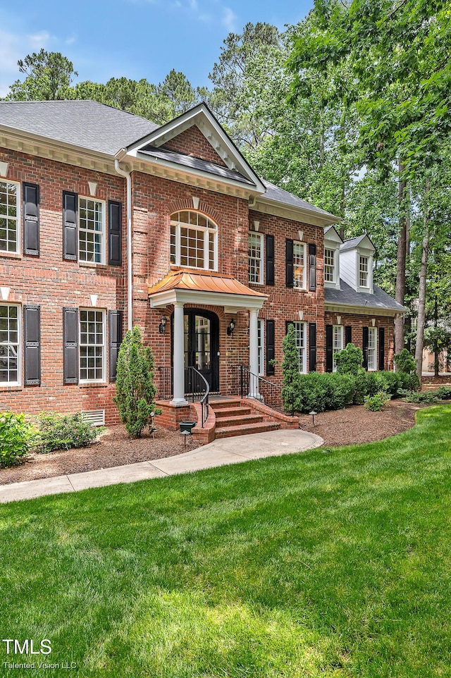 colonial inspired home featuring brick siding, a front lawn, and roof with shingles