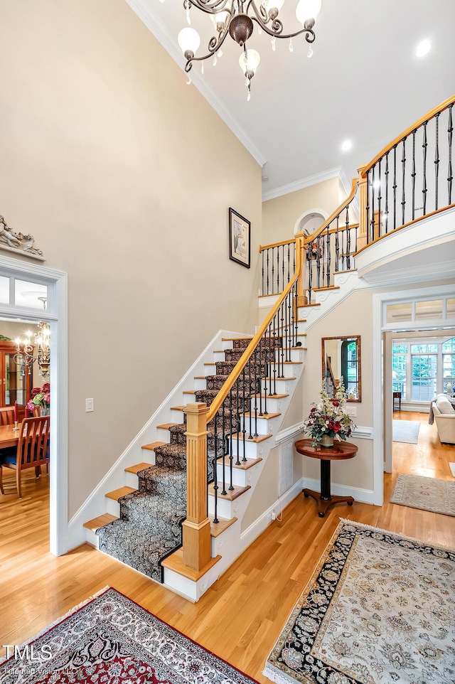 stairs with a chandelier, crown molding, wood finished floors, a towering ceiling, and baseboards