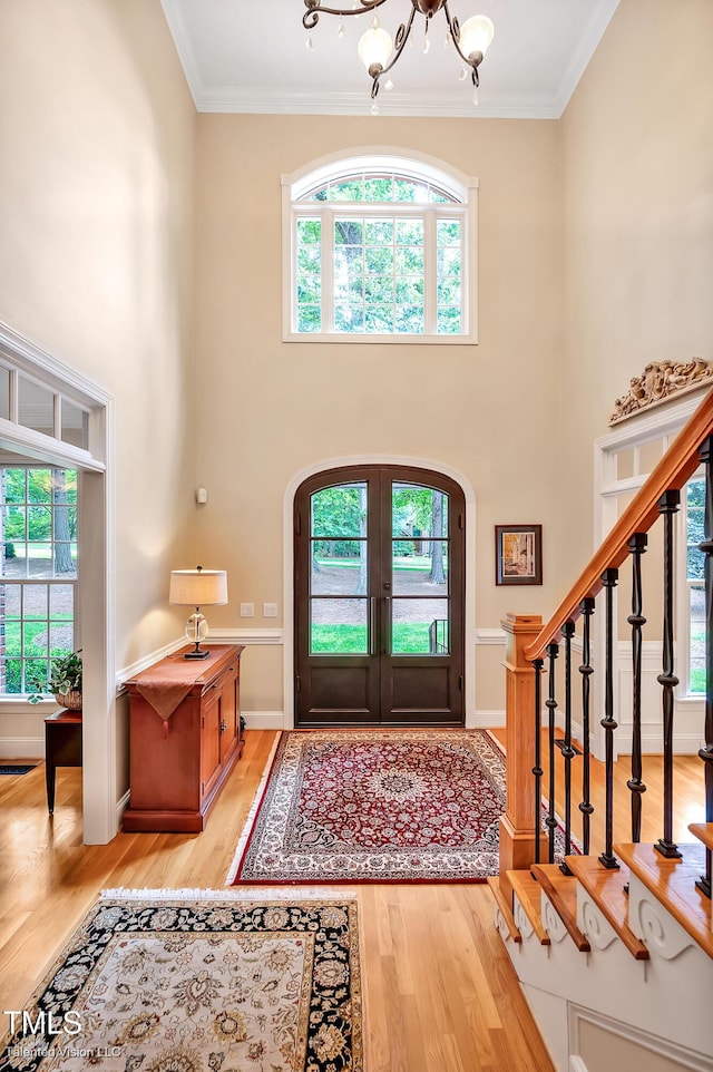 entryway with arched walkways, a chandelier, light wood-style floors, stairway, and ornamental molding