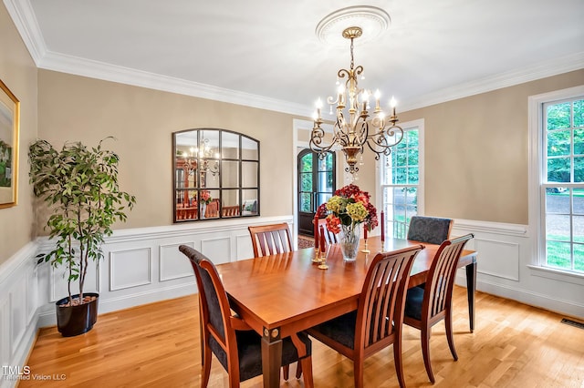dining space featuring a chandelier, healthy amount of natural light, light wood finished floors, wainscoting, and ornamental molding