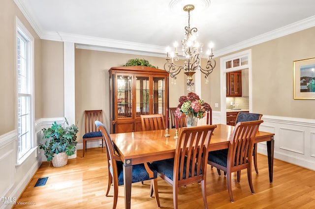 dining area featuring a chandelier, light wood-style flooring, crown molding, and a wainscoted wall