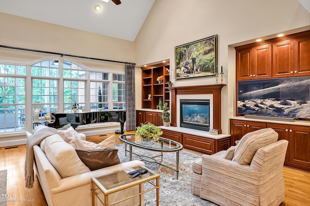 living area featuring high vaulted ceiling, light wood-type flooring, ceiling fan, and a glass covered fireplace