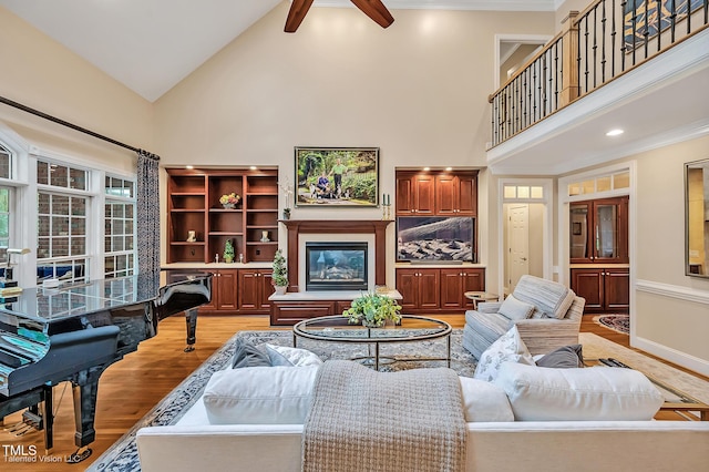living area with high vaulted ceiling, a ceiling fan, light wood-type flooring, baseboards, and ornamental molding