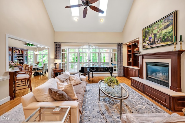 living room with high vaulted ceiling, ceiling fan, plenty of natural light, light wood-type flooring, and a glass covered fireplace