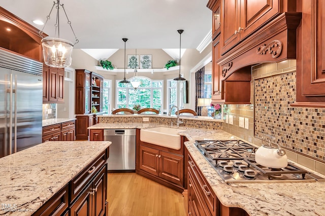 kitchen featuring appliances with stainless steel finishes, a sink, tasteful backsplash, pendant lighting, and light wood-type flooring