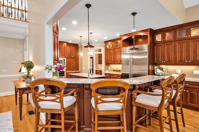 kitchen featuring built in appliances, a center island with sink, backsplash, recessed lighting, and light wood finished floors