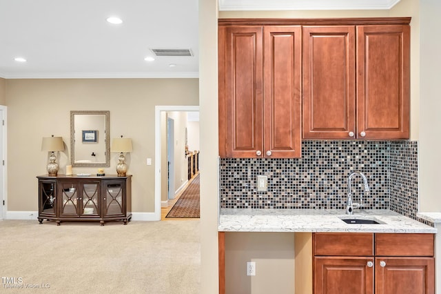 kitchen with a sink, ornamental molding, light colored carpet, baseboards, and light stone counters