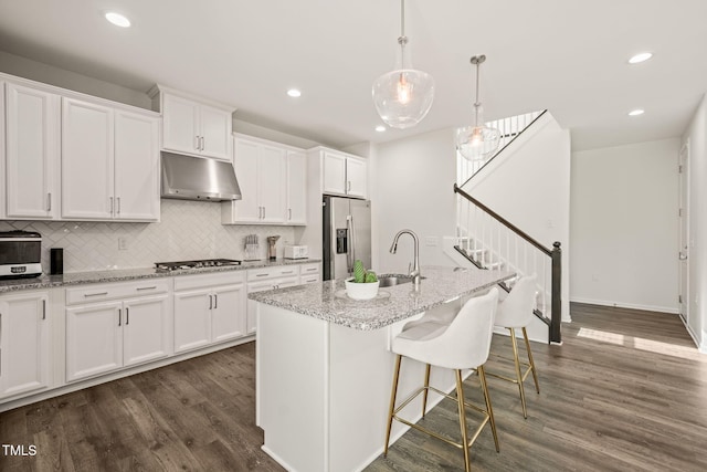 kitchen with stainless steel appliances, under cabinet range hood, a sink, white cabinetry, and recessed lighting