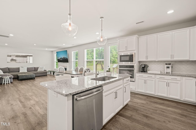 kitchen with stainless steel appliances, a sink, light wood-type flooring, decorative backsplash, and a kitchen island with sink