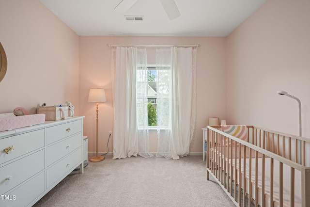 bedroom featuring light carpet, a nursery area, baseboards, and ceiling fan