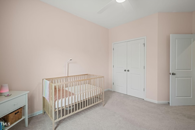 bedroom featuring carpet flooring, a closet, a crib, baseboards, and ceiling fan