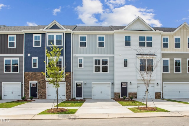 townhome / multi-family property with stone siding, board and batten siding, driveway, and an attached garage
