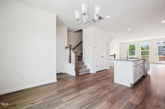 kitchen with a sink, wood finished floors, dishwasher, light stone countertops, and a chandelier