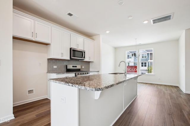 kitchen featuring appliances with stainless steel finishes, a sink, white cabinets, dark wood-style floors, and a kitchen island with sink