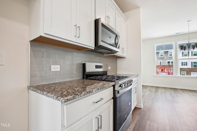 kitchen with appliances with stainless steel finishes, dark stone counters, backsplash, white cabinetry, and wood finished floors