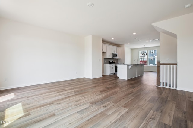 unfurnished living room with wood finished floors, a sink, recessed lighting, and baseboards