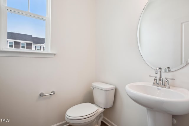 half bathroom with baseboards, toilet, and a sink