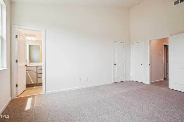 unfurnished bedroom with carpet flooring, a towering ceiling, baseboards, and ensuite bathroom