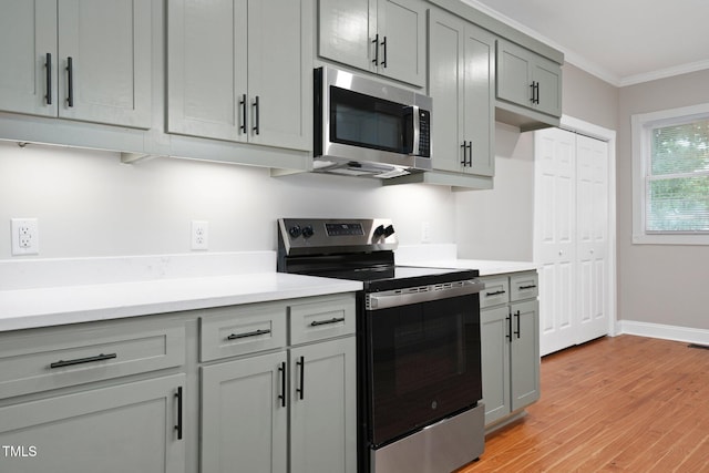 kitchen featuring appliances with stainless steel finishes, gray cabinets, crown molding, light wood-style flooring, and light countertops
